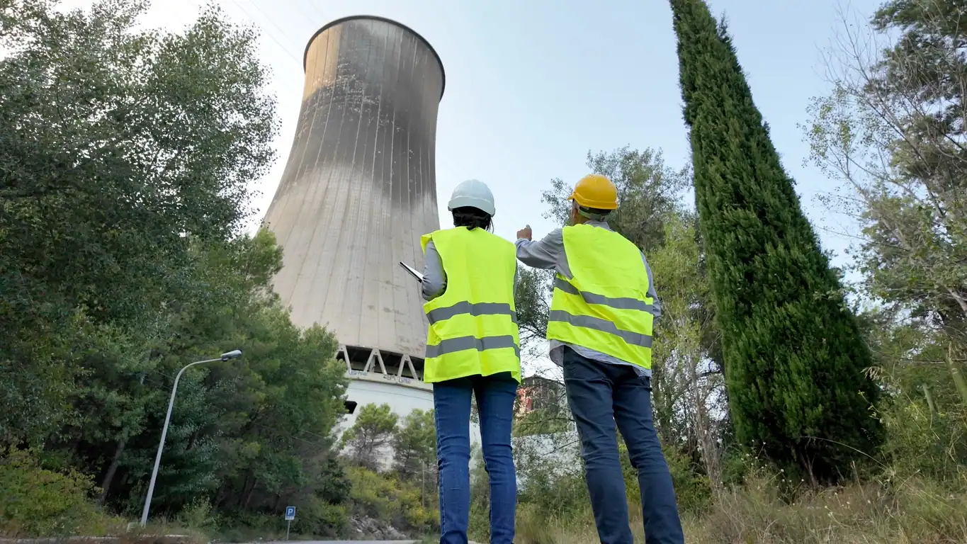 Environmental engineers reviewing plans near a nuclear power plant cooling tower